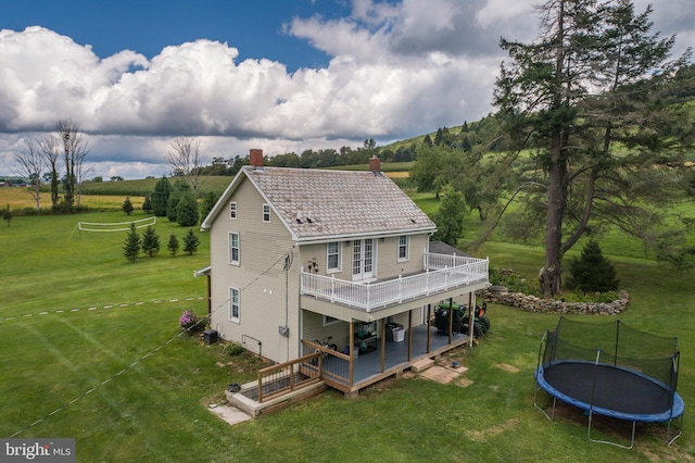 back of house with a trampoline, a yard, a chimney, and a wooden deck