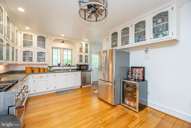 kitchen featuring beverage cooler, stainless steel appliances, white cabinets, dark countertops, and glass insert cabinets