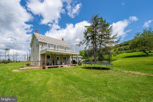 back of property with a balcony, a lawn, a wooden deck, and a trampoline