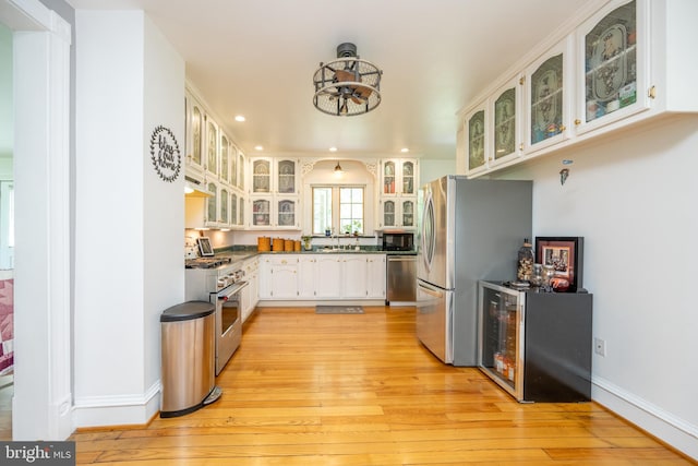 kitchen with light wood-type flooring, wine cooler, sink, appliances with stainless steel finishes, and white cabinets