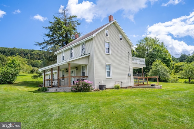 rear view of house featuring covered porch, central AC unit, a chimney, and a lawn