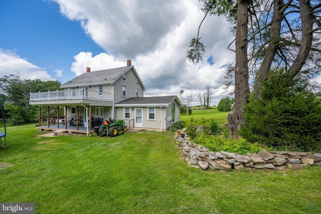 back of house featuring a trampoline, a lawn, a chimney, and a wooden deck