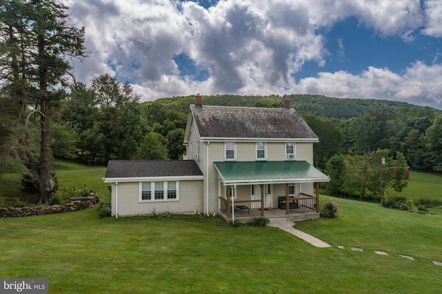 back of house featuring a chimney, a wooded view, a porch, and a lawn