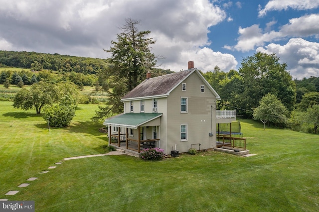 back of property with a forest view, a chimney, cooling unit, and a yard