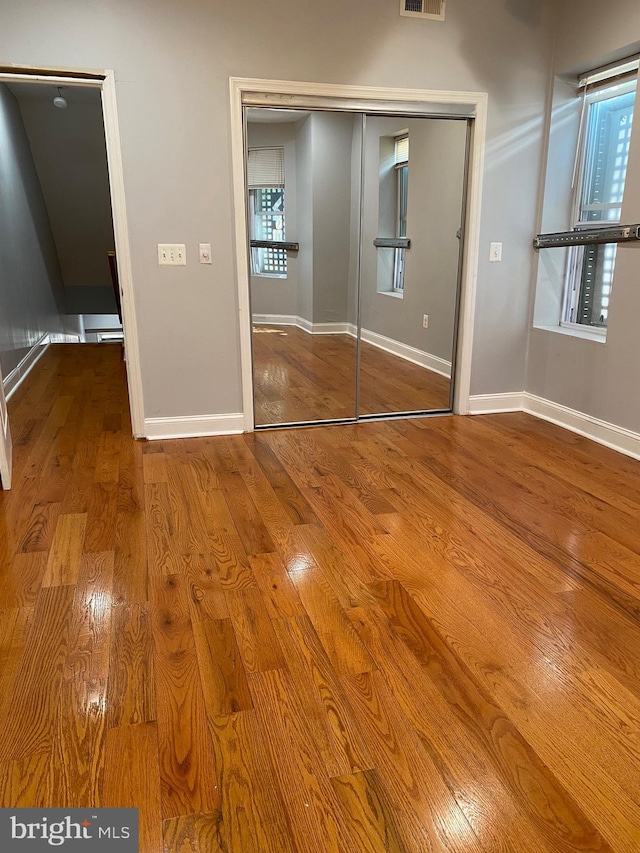 unfurnished bedroom with a closet, wood finished floors, visible vents, and baseboards