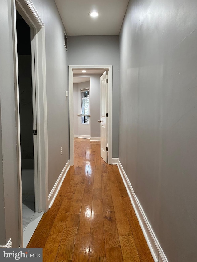 hall with light wood-style flooring, visible vents, and baseboards