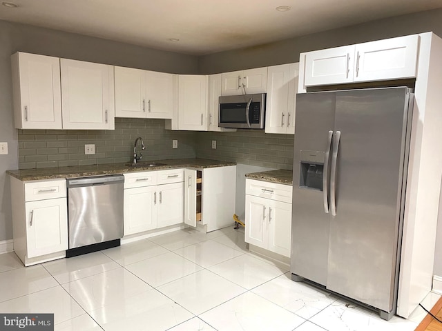 kitchen featuring appliances with stainless steel finishes, white cabinetry, a sink, and dark stone countertops