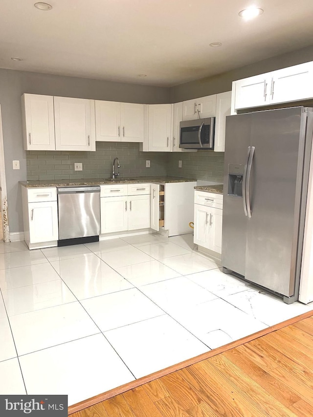 kitchen with dark countertops, appliances with stainless steel finishes, white cabinets, and backsplash