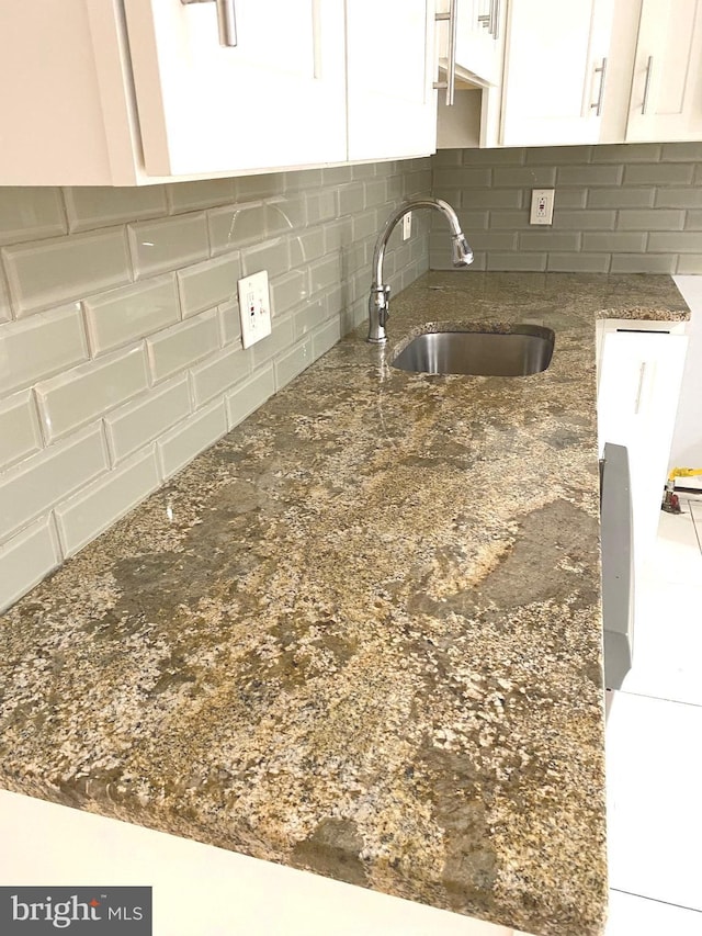 kitchen featuring tasteful backsplash, dark stone counters, white cabinets, and a sink