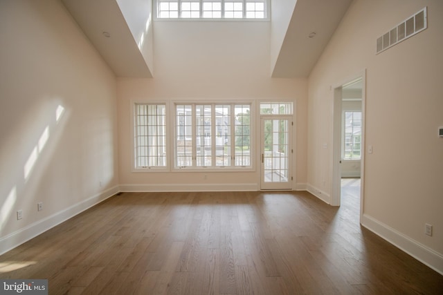 interior space featuring a towering ceiling, a healthy amount of sunlight, and dark hardwood / wood-style flooring