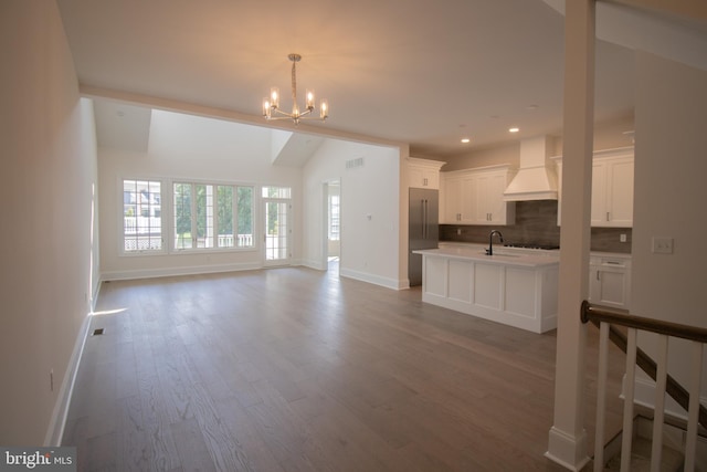 unfurnished living room featuring an inviting chandelier, vaulted ceiling, light hardwood / wood-style floors, and sink