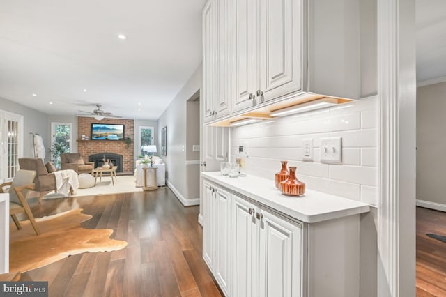 kitchen featuring ceiling fan, a fireplace, dark wood-type flooring, and white cabinetry