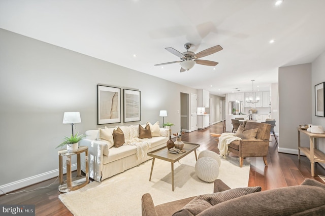 living room featuring ceiling fan with notable chandelier and dark wood-type flooring