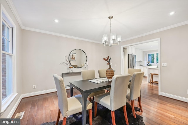 dining space with ornamental molding, a notable chandelier, a wealth of natural light, and light hardwood / wood-style floors