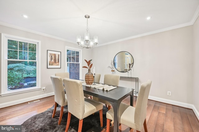 dining space with wood-type flooring, ornamental molding, and a notable chandelier