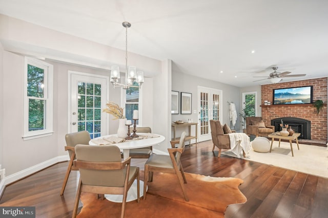 dining room with ceiling fan with notable chandelier, hardwood / wood-style flooring, and a fireplace