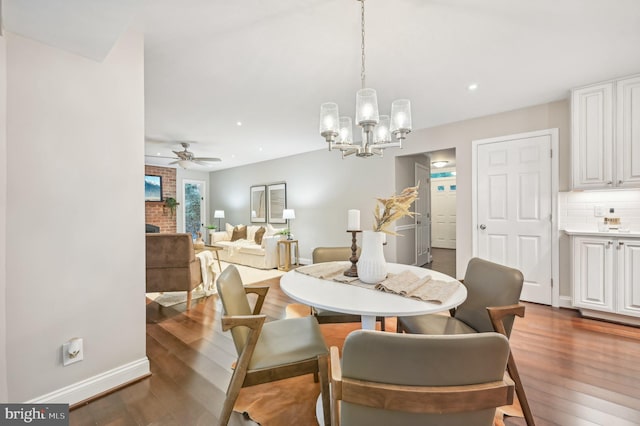 dining room with a brick fireplace, ceiling fan with notable chandelier, and dark hardwood / wood-style floors