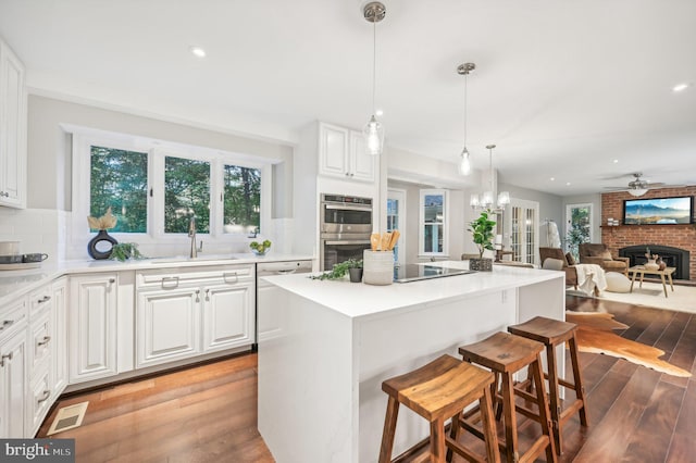 kitchen featuring a brick fireplace, light hardwood / wood-style floors, sink, white cabinets, and double oven