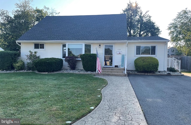 view of front of home featuring a front lawn, roof with shingles, fence, and aphalt driveway