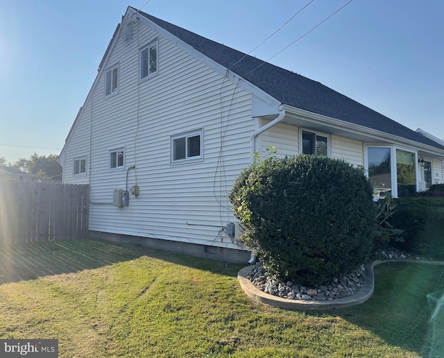 view of property exterior featuring a shingled roof, a lawn, and fence