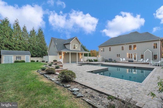 rear view of house with a patio, a lawn, a fenced in pool, and a storage shed