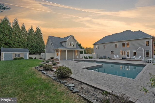 pool at dusk with a storage unit, a yard, and a patio