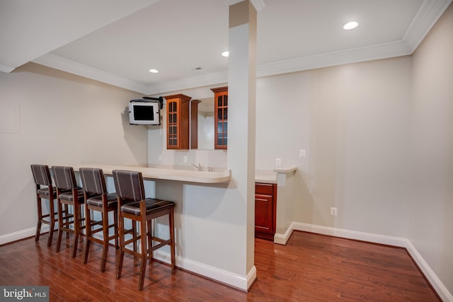 kitchen with a kitchen breakfast bar, dark hardwood / wood-style floors, kitchen peninsula, and crown molding