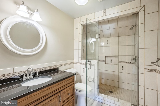 bathroom with tile patterned flooring, vanity, a shower with shower door, toilet, and tile walls