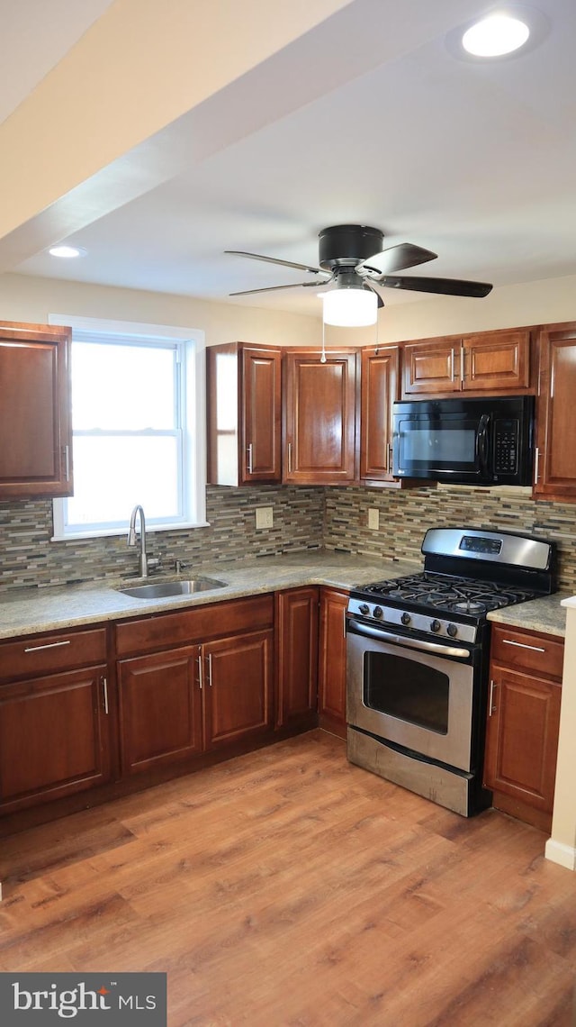 kitchen featuring tasteful backsplash, black microwave, light wood-type flooring, gas stove, and a sink