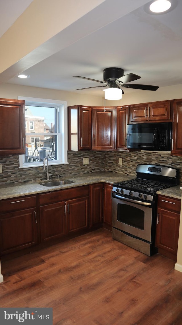 kitchen with black microwave, dark wood finished floors, decorative backsplash, gas stove, and a sink