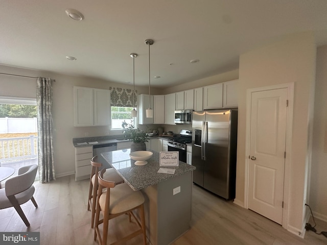 kitchen with appliances with stainless steel finishes, light wood-type flooring, a kitchen island, and a wealth of natural light