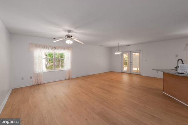 unfurnished living room featuring ceiling fan with notable chandelier, french doors, hardwood / wood-style floors, and sink