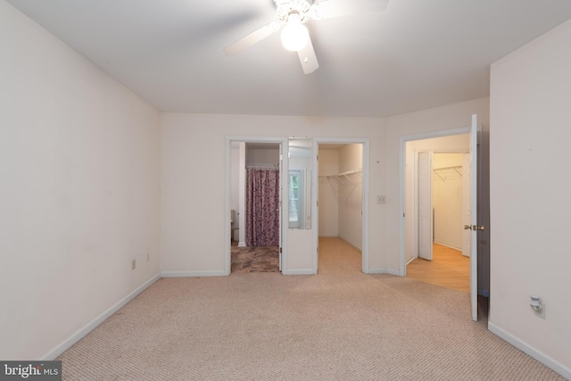 unfurnished bedroom featuring a walk in closet, ceiling fan, light colored carpet, and a closet