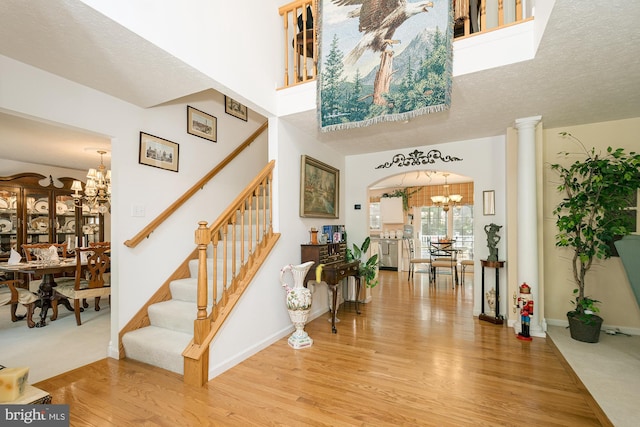 entrance foyer with light wood-type flooring, ornate columns, an inviting chandelier, and a textured ceiling