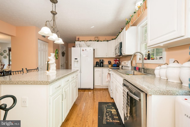 kitchen with light wood-type flooring, decorative light fixtures, sink, appliances with stainless steel finishes, and a breakfast bar area