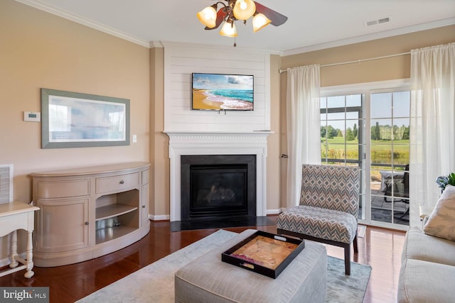 living room featuring a large fireplace, visible vents, a ceiling fan, ornamental molding, and dark wood finished floors