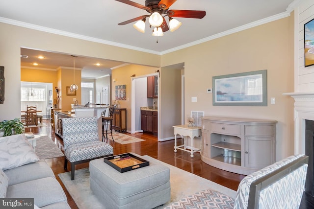 living room featuring dark wood-style flooring, a fireplace, a ceiling fan, baseboards, and crown molding