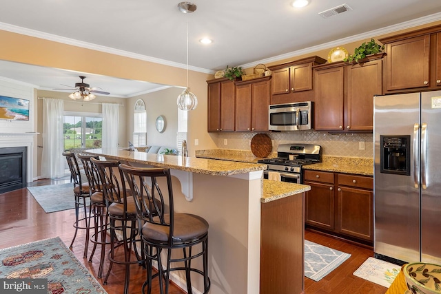 kitchen featuring stainless steel appliances, visible vents, a kitchen breakfast bar, hanging light fixtures, and brown cabinetry