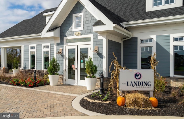 view of exterior entry featuring french doors and roof with shingles