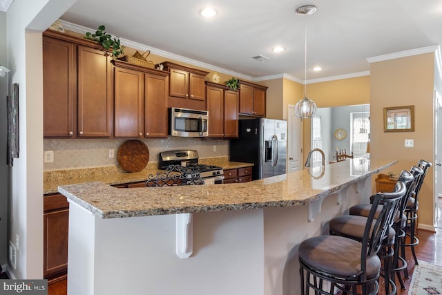 kitchen featuring a breakfast bar area, a kitchen island with sink, stainless steel appliances, visible vents, and brown cabinetry