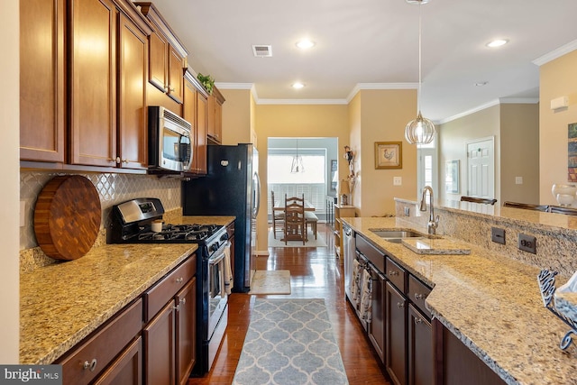 kitchen with decorative light fixtures, stainless steel appliances, decorative backsplash, a sink, and light stone countertops