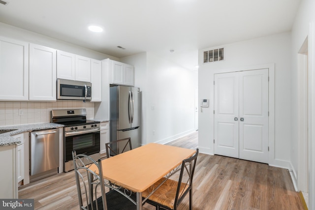 kitchen with appliances with stainless steel finishes, light stone counters, tasteful backsplash, white cabinets, and light wood-type flooring