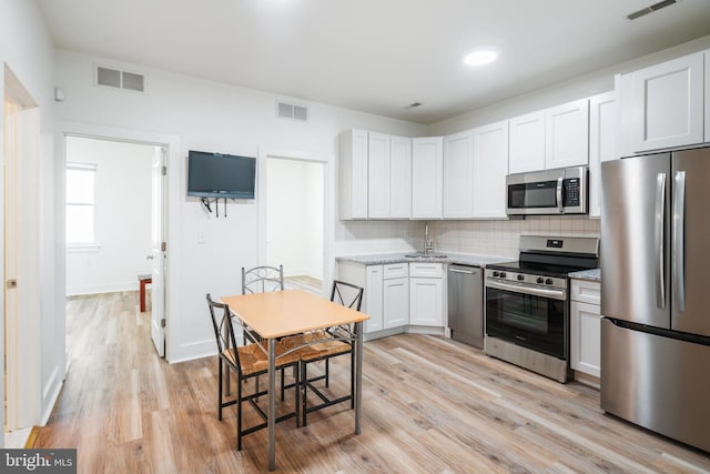 kitchen with light hardwood / wood-style floors, tasteful backsplash, white cabinetry, stainless steel appliances, and light stone countertops