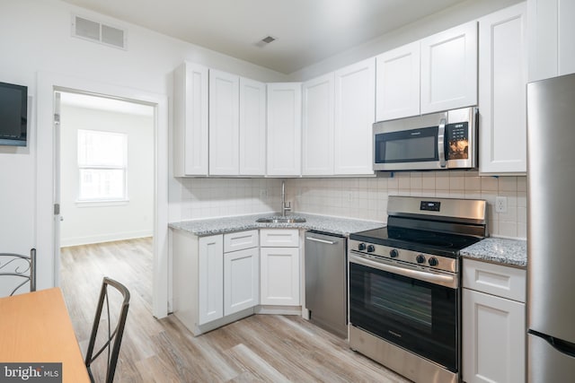 kitchen with light stone counters, light hardwood / wood-style flooring, stainless steel appliances, and white cabinetry