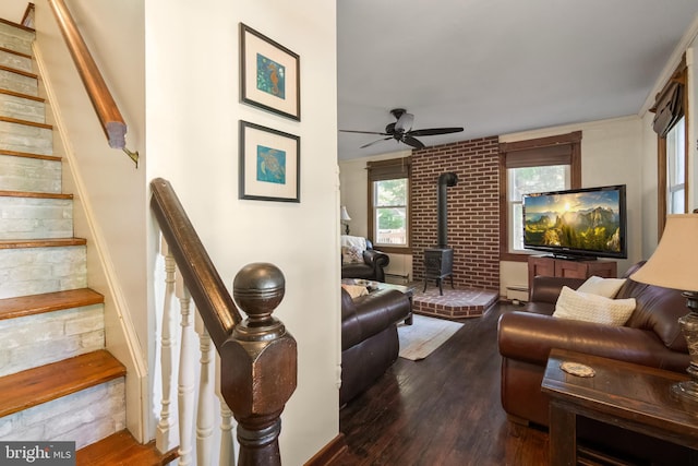 living room with a baseboard heating unit, dark wood-type flooring, ceiling fan, and a wood stove