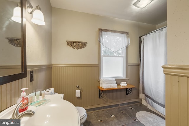 full bath with a shower with curtain, wainscoting, a sink, and toilet