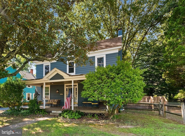 view of front of home featuring covered porch, a chimney, and fence