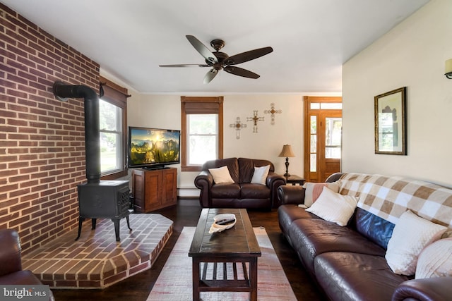 living room with brick wall, dark hardwood / wood-style flooring, a wood stove, a baseboard heating unit, and ceiling fan