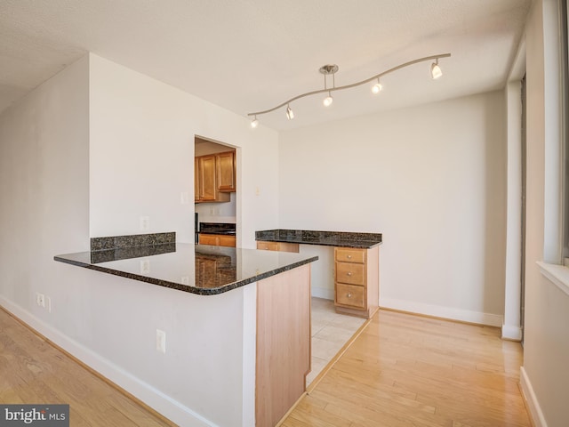 kitchen featuring dark stone countertops, a textured ceiling, light hardwood / wood-style floors, kitchen peninsula, and a breakfast bar