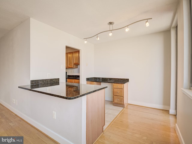 kitchen featuring dark stone counters, baseboards, a peninsula, and light wood finished floors